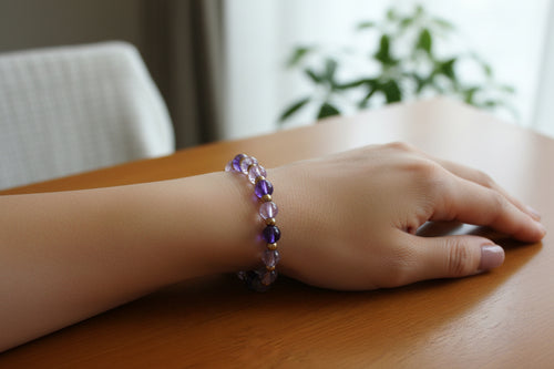 A beaded stretch bracelet with faceted purple glass beads and small metallic gold spacer beads, displayed on a textured white fabric background.