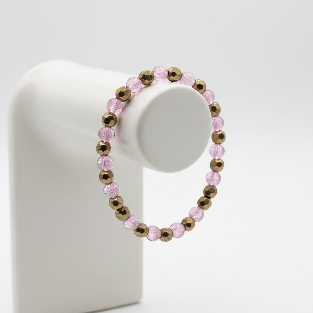 A beaded stretch bracelet made of pink faceted beads and metallic bronze spacer beads, displayed on a textured beige fabric background.