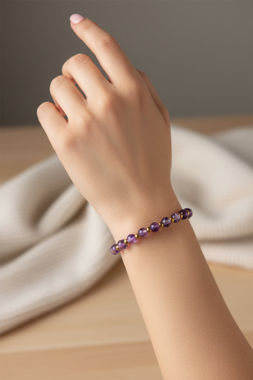A beaded stretch bracelet featuring purple translucent beads and small metallic gold spacer beads, displayed on a soft, textured white faux fur surface.